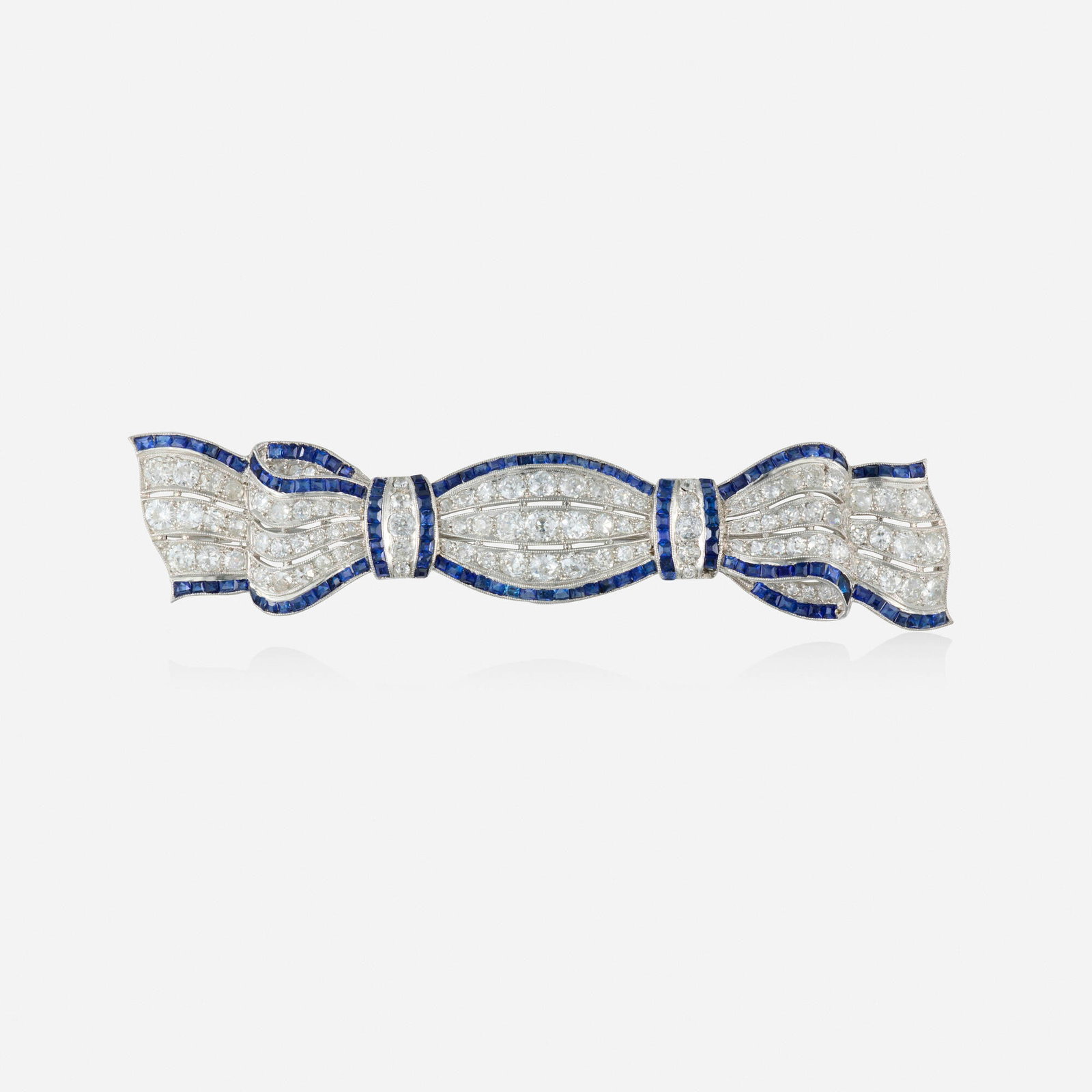 Art Deco, Synthetic sapphire, diamond, and platinum brooch: Art Deco Synthetic sapphire, diamond, and platinum brooch The bow set with French and square-cut synthetic sapphires and old mine-cut diamonds Platinum 3.25 x 0.75 in; Gross weight 9.7 dwts This work 
