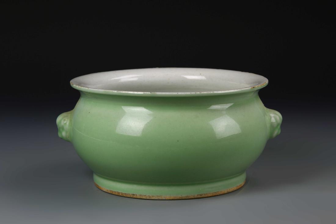 Chinese Apple Green Glazed Censer: China, Qing Dynasty, apple-green glazed censer, flared and rounded lipped rim, animal head ears, round, squashed body on footed base, plain white interior with green glaze on exterior. Diameter 10 in.