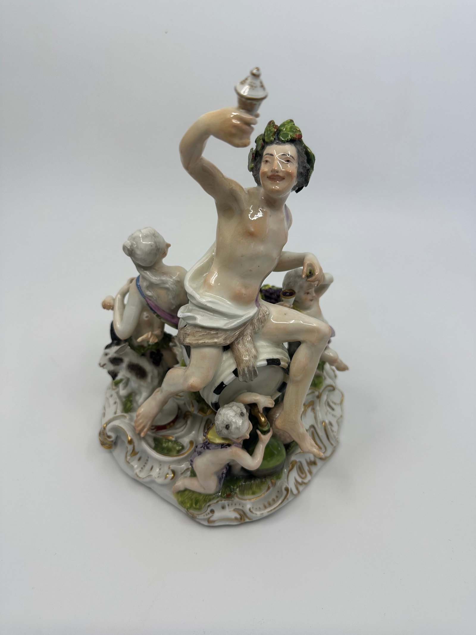 A Meissen group of Bacchus and attendants: A Meissen group of Bacchus and attendants Late 18th century, BLUE CROSSED SWORDS MARK, INCISED 2202, PRESSNUMMER 51The God wearing a leopord's pelt, seated on a barrel holding a bunch of grapes and a 