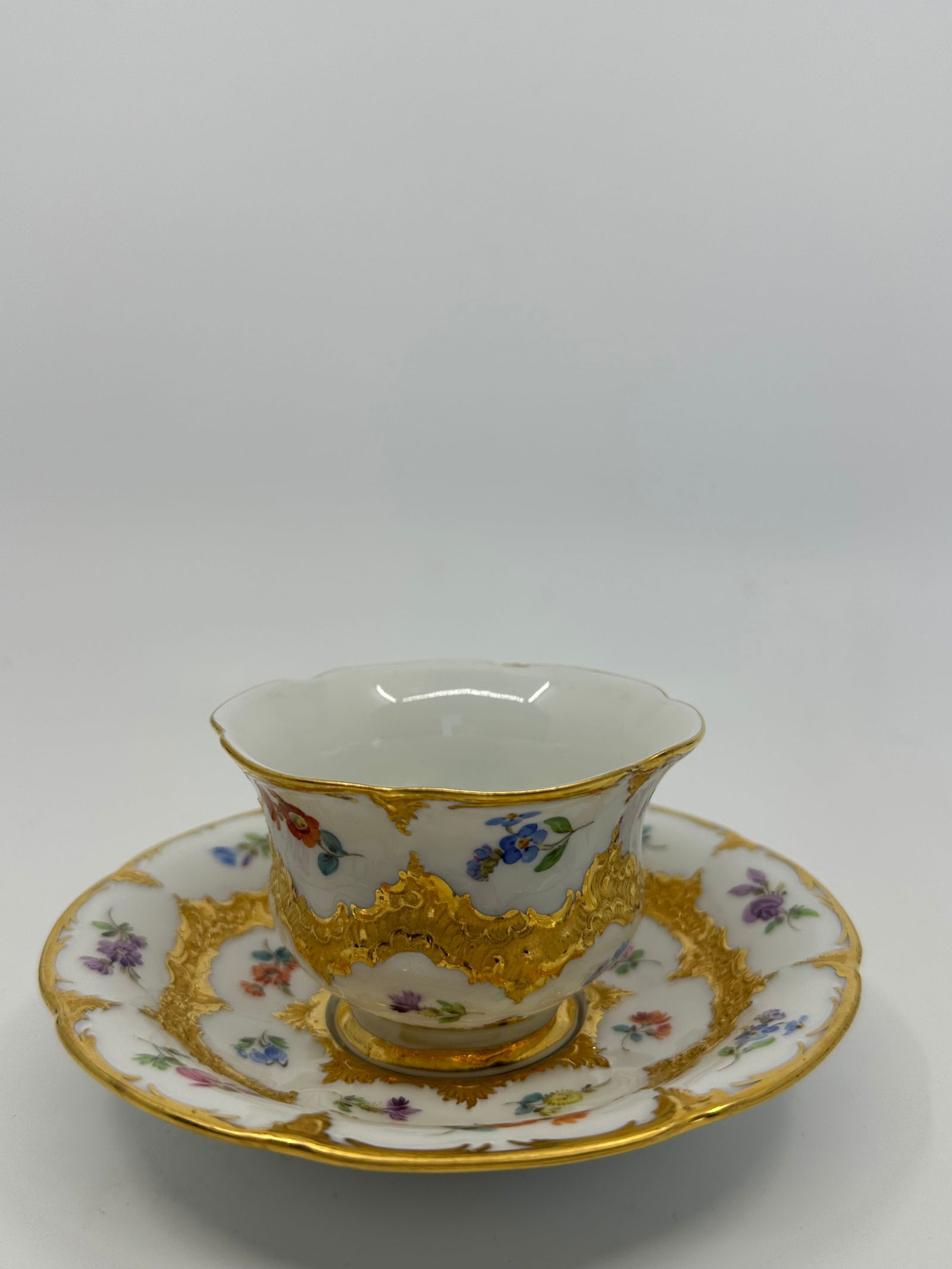 Antique Meissen B Form Strewn Flowers Gold Gilt Tea Cup & Saucer Set: Fine antique Meissen porcelain tea cup and saucer plate set, gold decorated with embossed ornaments of floral motifs. In the middle assorted bouquets of multicolored flowers. This Meissen saucer and c