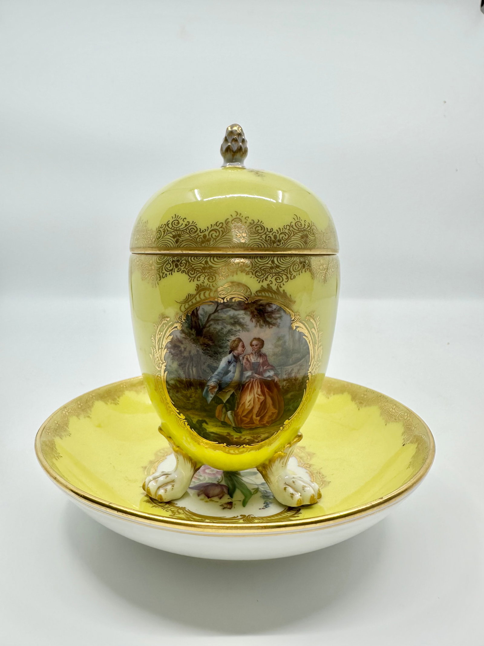 Meissen Chocolate Cup Saucer And Lid, ca. 1890: The Meissen porcelain chocolate cup and saucer with lid is painted with cartouche of flower bouquets, gilded scrollwork and stands on lion feet, Meissen cross swords to base. Meissen c. 1890 h. 12.5cm