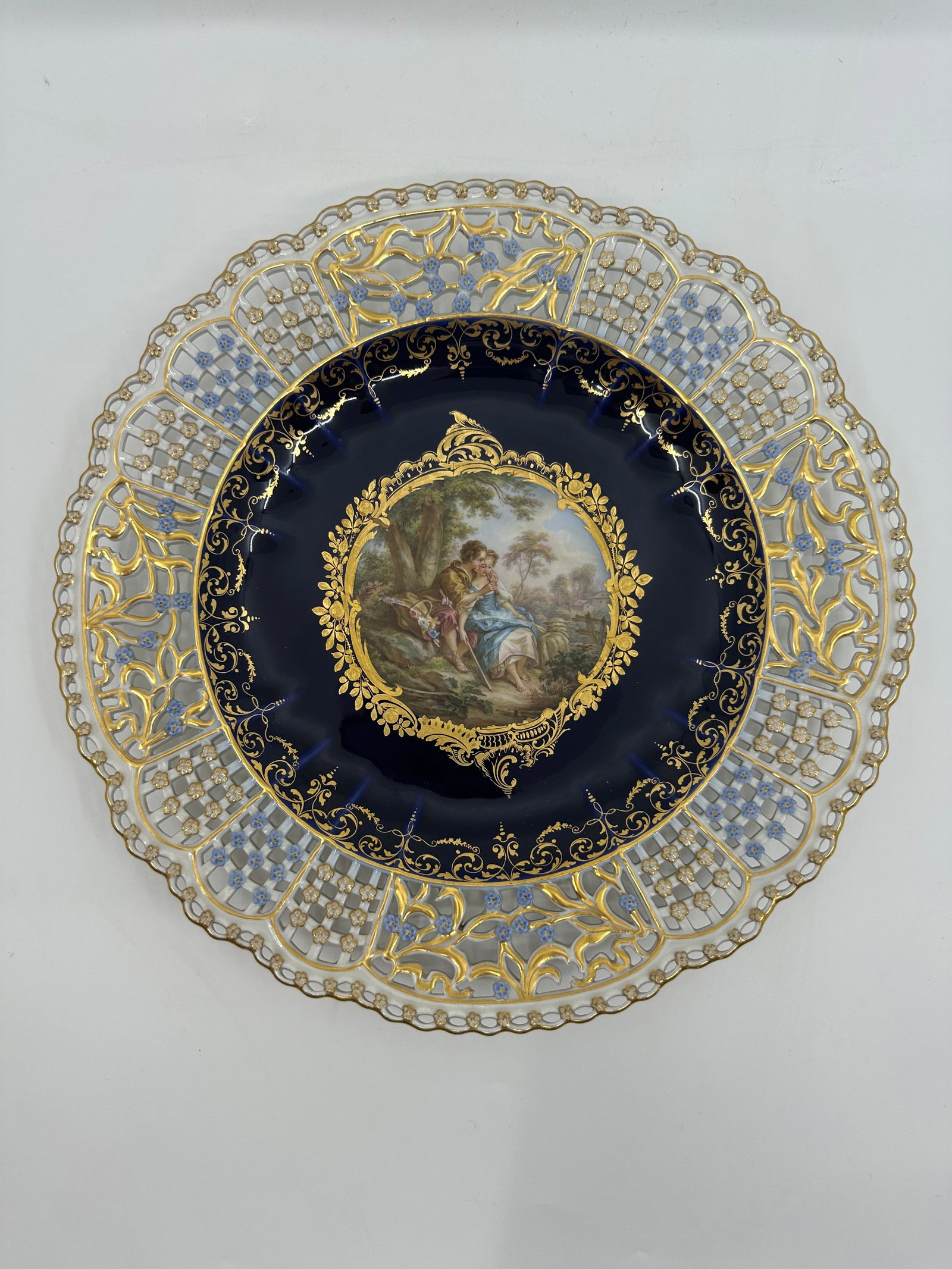 ANTIQUE MEISSEN PORCELAIN COBALT-BLUE GROUND RETICULATED CABINET PLATE: DescriptionANTIQUE MEISSEN PORCELAIN COBALT-BLUE GROUND RETICULATED CABINET PLATE. LATE 19TH CENTURY, BLUE CROSSED SWORDS MARKS, VARIOUS IMPRESSED NUMERALS. Finely painted Watteau scene 10 3/8 in. (26