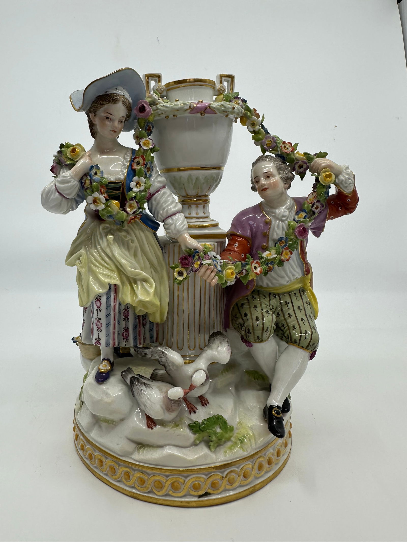 Meissen Porcelain Figural Group: late19th century; underglaze blue crossed swords mark, incised "F88," depicting a couple and young girl, seated around an urn and column, holding a floral garland, 8 1/4 in. H.