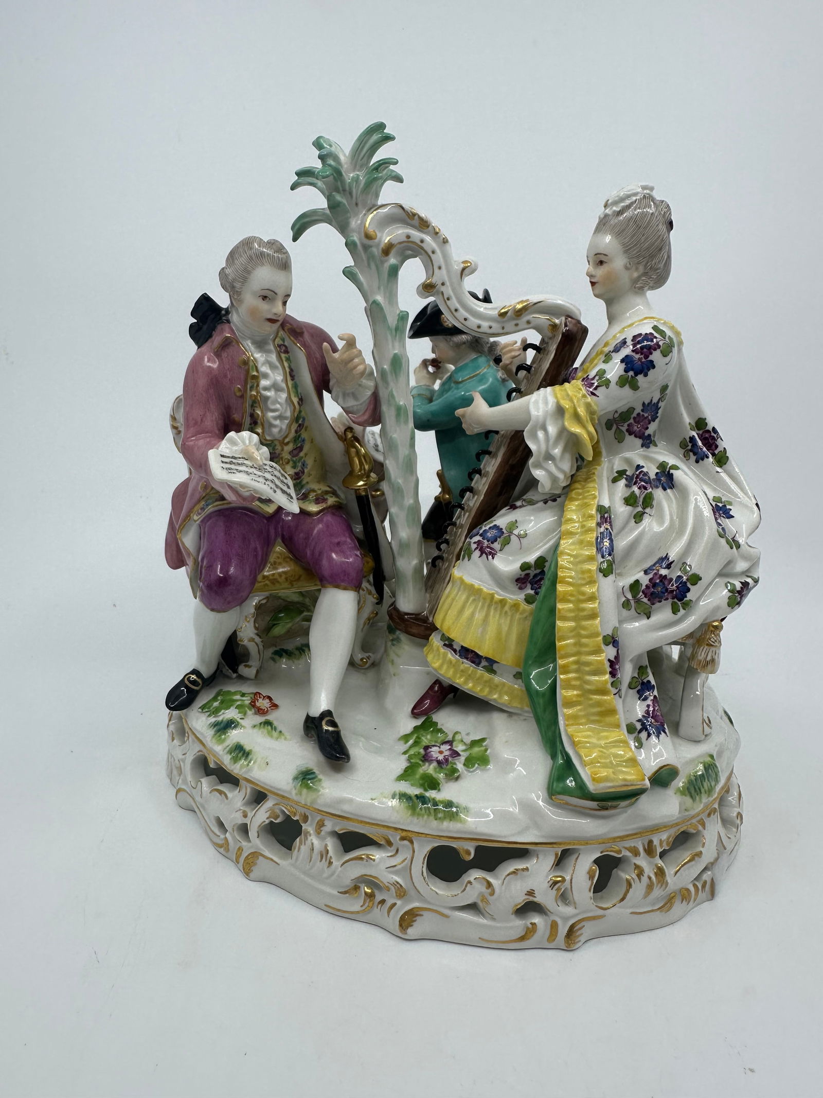 Meissen Porcelain Musical Figural Group w/ Harpist: Meissen polychrome decorated porcelain figural group, depicting musicians in Continental dress, the woman playing a harp, a man holding her sheet music, and a boy playing the flute, rising on an oval