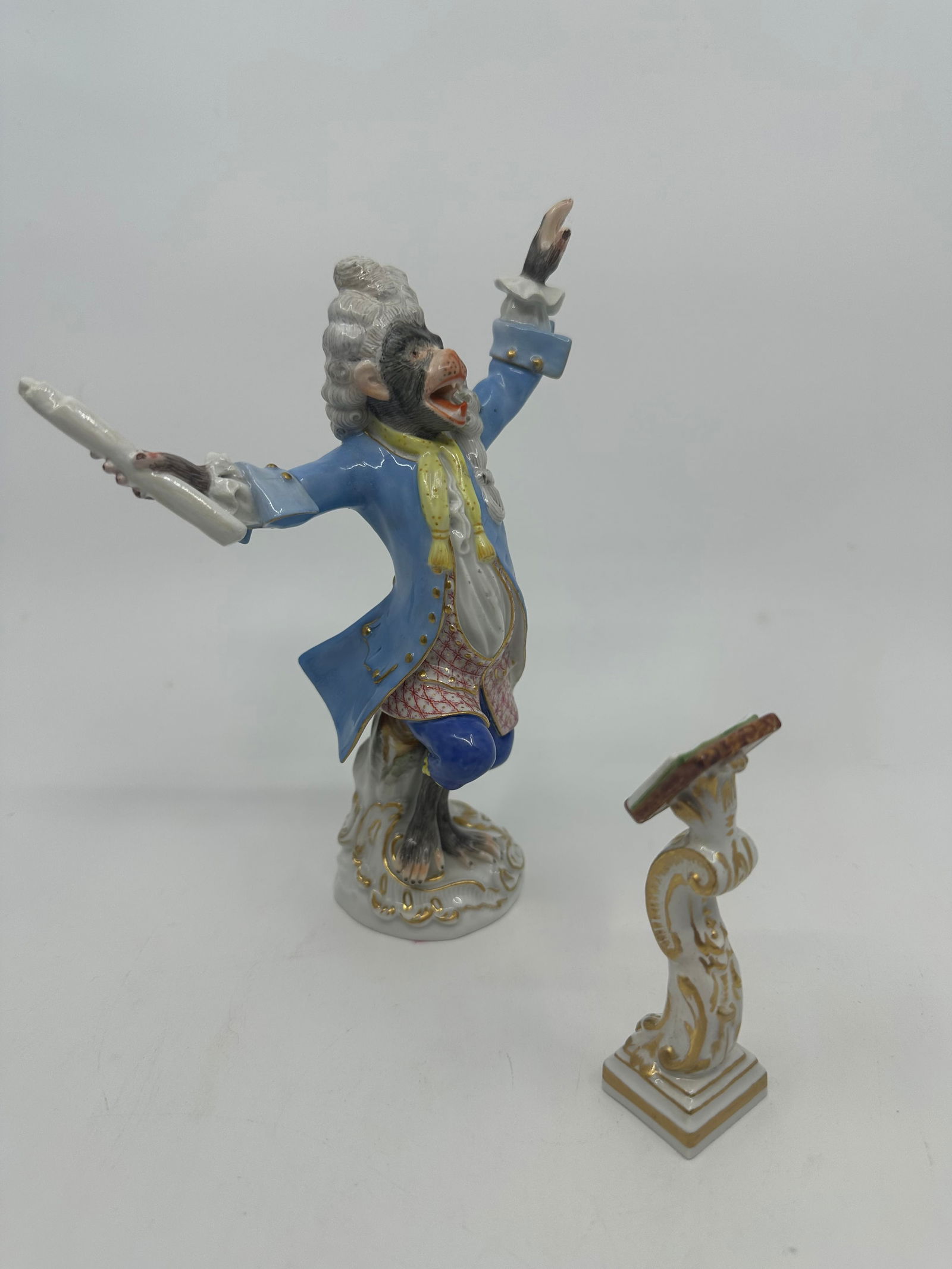 MEISSEN PORCELAIN MONKEY ORCHESTRA CONDUCTOR & MUSIC STAND: German Meissen hand-painted porcelain figure, the conductor with music stand from the monkey band, after the model by Johann Joachim Kandler (1706-1775), 20th c., depicted in a powdered wig, pale blue