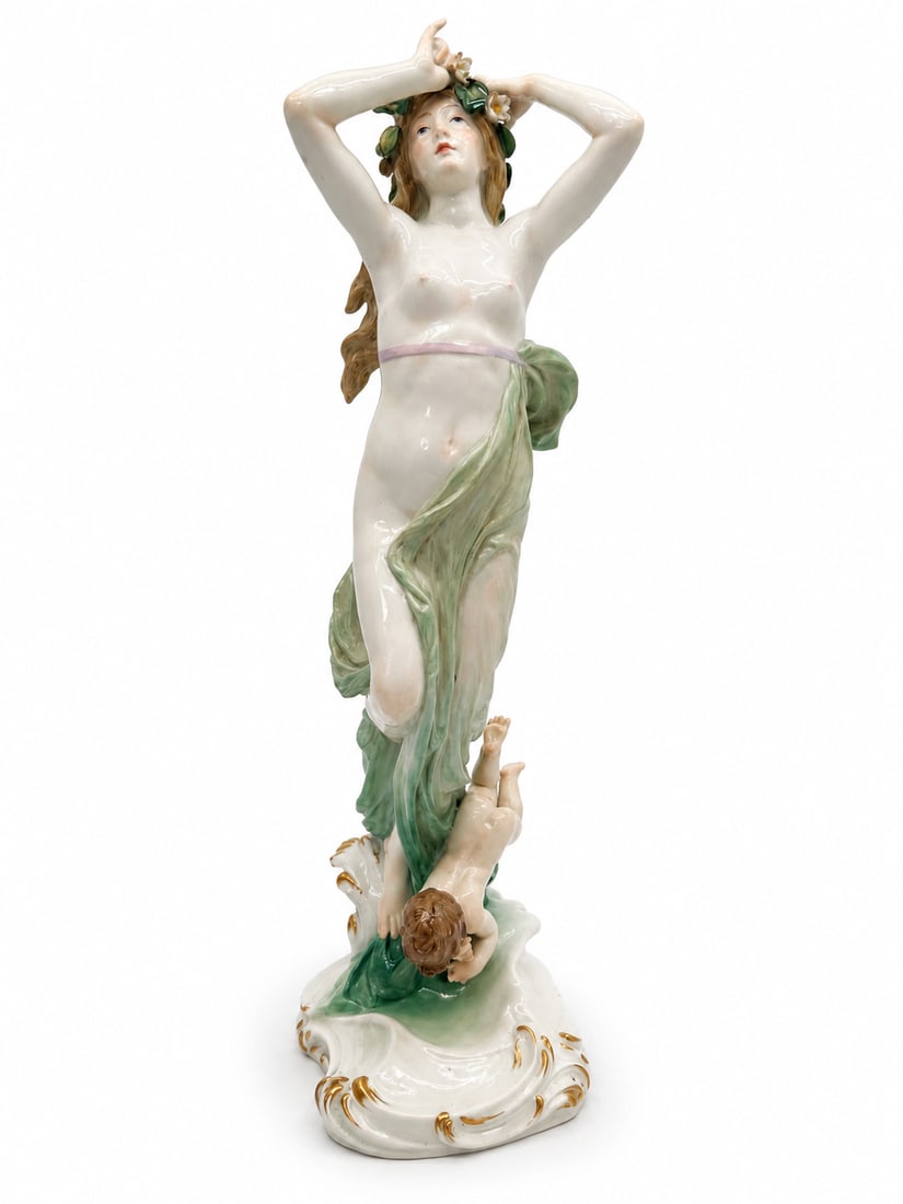 A MEISSEN FIGURE GROUP OF A NYMPH AND PUTTO: A MEISSEN FIGURE GROUP OF A NYMPH AND PUTTOLATE 19TH/20TH CENTURY, BLUE CROSSED SWORDS MARK, INCISED MODEL NO. R 124, IMPRESSED 137 AND BLACK 74.The scantily clad maiden modeled standing atop the cres