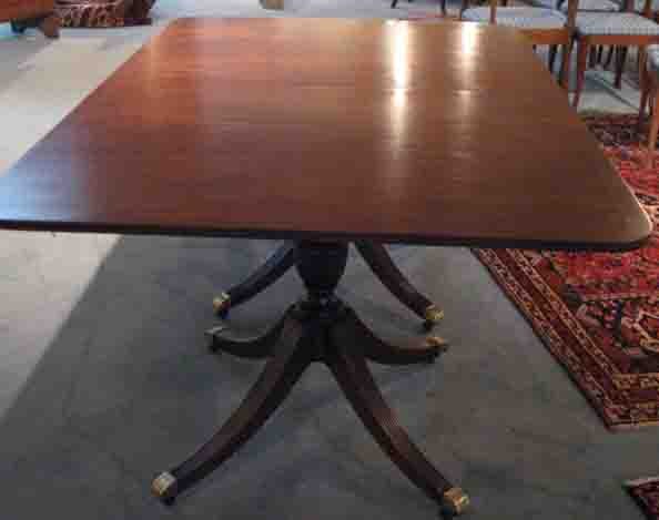 A Baker Mahogany Dining Table,: in the Duncan Phyfe taste, having string and banded inlay to the top, over two turned columns, each with four curved and reeded legs ending in brass caps on casters. 29 1/2" high, 46" wide 68" long, t