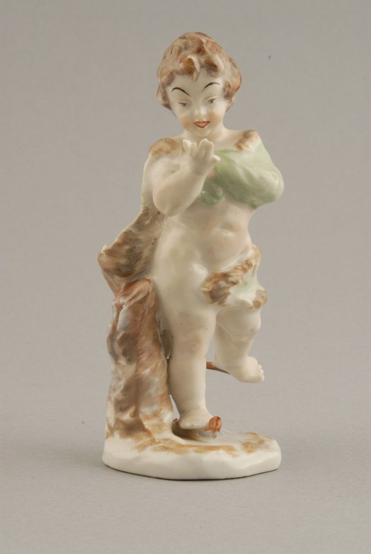 A Ginori/Capo-di-Monte Porcelain Figure of a cheru: of a cherub on ice skates, in a fur trimmed green drape, with a blue underglaze mark to the bottom. 5" high. One broken finger and one broken ice skate.