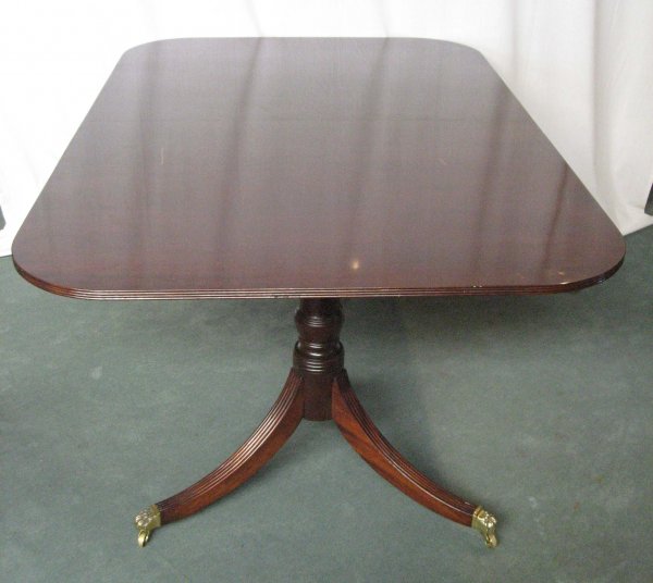 A Centennial Dining Table,: mahogany in the Duncan Phyfe taste, having a reeded edge to the rounded corner top, with two leaves, one original, one added, resting on two turned columns, tripod reeded legs ending in brass paw feet
