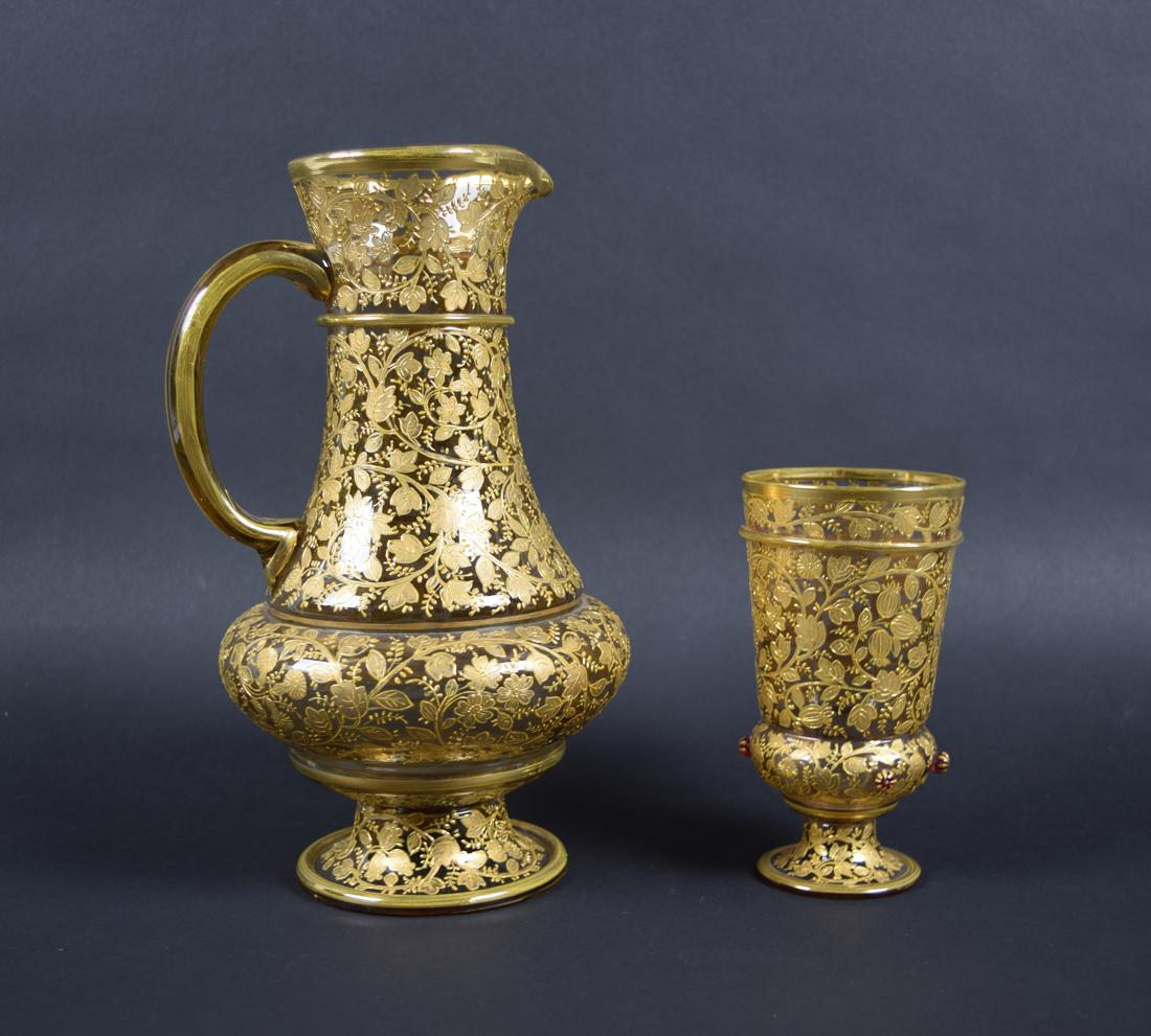 St. Louis Style Chalice and Pitcher with Gold Accent: Set of gilt St. Lewis style Chalice and pitcher. Each is constructed of clear crystal with heavy gold floral pattern accenting, making them appear translucent. Cup features red chrystal berry accentin