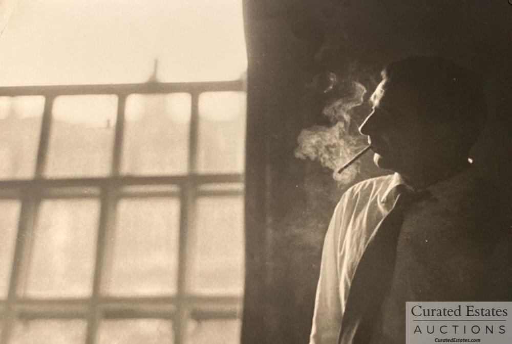 Black and White Photo of Robert Capa in 1953: Black and White Photo of Robert Capa in 1953 visiting John Huston in the Hospital smoking a cigarette. Stamped on verso: Ernest Haas - Magnum Photo Provenance: The Estate of John and Elaine Steinbeck