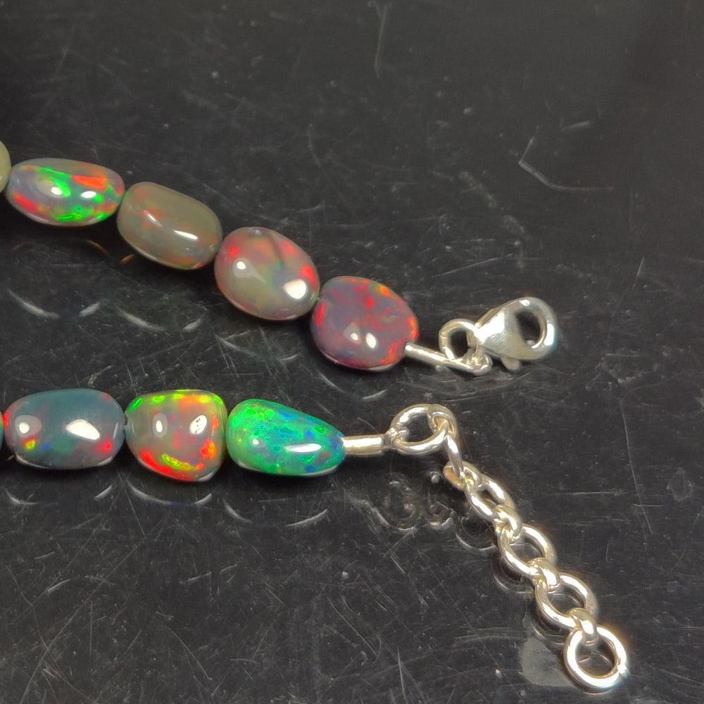 29.62 Ct Natural Black Flashing Fire Opal Dumble Beads Bracelet Ready Wear: Weight - 29.62 Ct / Size - 8.8x7.2 - 10.8x7.9 mm / 16 Pc's / Shape - Dumble Beads / Color - Black / Clarity - Translucent / Origin - Ethiopia / Treatment - Color Smoked