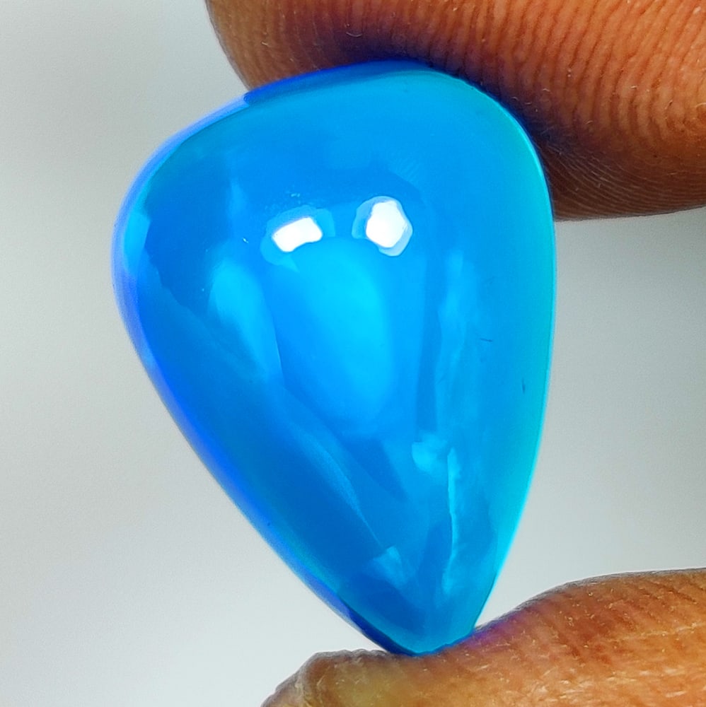 4.56 Ct Natural Blue Flashing Fire Opal Pear Cab: Weight - 4.56 Ct / Dimensions -15.20 x 10.90 x 6.90 mm / Shape - Pear Cab / Color - Black / Clarity - Translucent / Origin - Ethiopia / Treatment - Heated