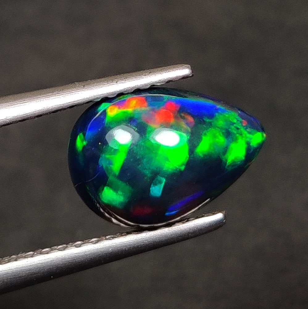 1.30 Ct Natural Black Flashing Fire Opal Pear Cab: Weight - 1.30 Ct / Dimensions - 10.20 x 7.10 x 4.30 mm / Shape - Pear Cab / Color - Black / Clarity - Translucent / Origin - Ethiopia / Treatment - Color Smoked