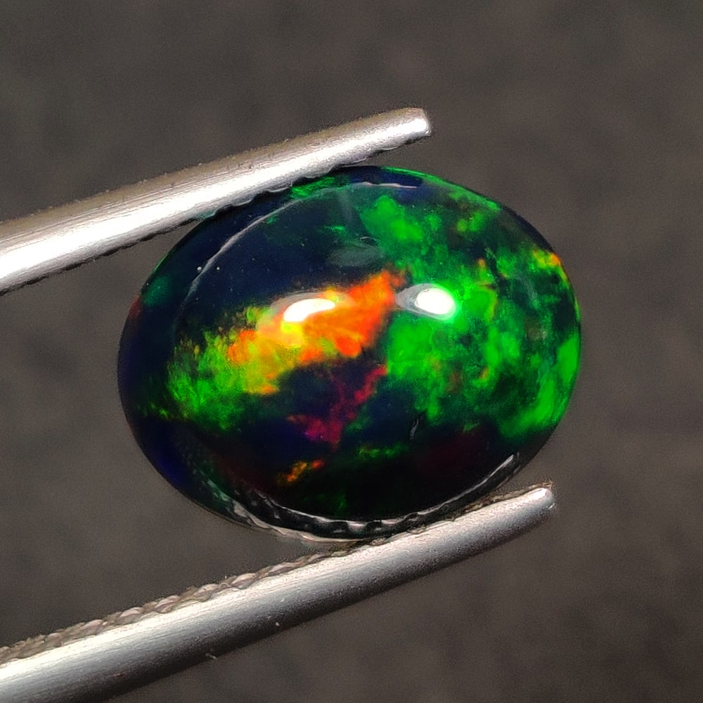 1.32 Ct Natural Black Flashing Fire Opal Oval Cab: Weight - 1.32 Ct / Size - 9.90 x 7.90 x 4.20 mm / Shape - Oval Cab / Color - Black / Transparency - Translucent / Origin - Ethiopia / Treatment - Color Smoked