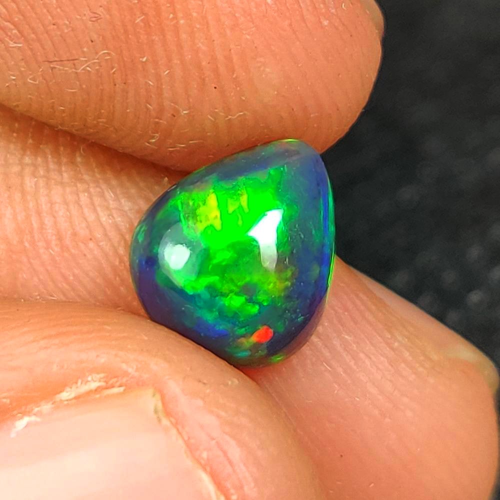 1.22 Ct Natural Black Flashing Fire Opal Pear Cab: Weight - 1.22 Ct / Dimensions - 8.90 x 7.70 x 3.90 mm / Shape - Pear Cab / Color - Black / Clarity - Translucent / Origin - Ethiopia / Treatment - Color Smoked