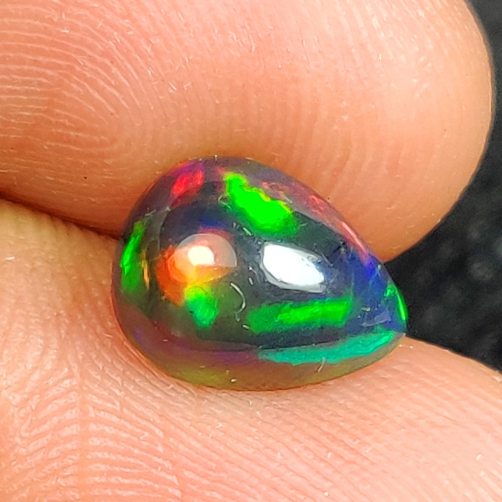 2.01 Ct Natural Black Flashing Fire Opal Pear Cab: Weight - 2.01 Ct / Dimensions - 10.20 x 8.20 x 5.20 mm / Shape - Pear Cab / Color - Black / Clarity - Translucent / Origin - Ethiopia / Treatment - Color Smoked