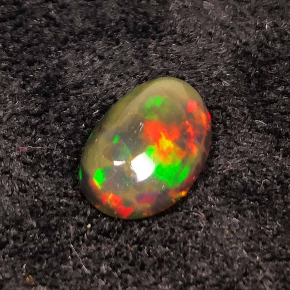 1.55 Ct Natural Black Flashing Fire Opal Oval Cab: Weight - 1.55 Ct / Dimensions - 10.80 x 7.50 x 4.00 mm / Shape - Oval Cab / Color - Black / Clarity - Translucent / Origin - Ethiopia / Treatment - Color Smoked