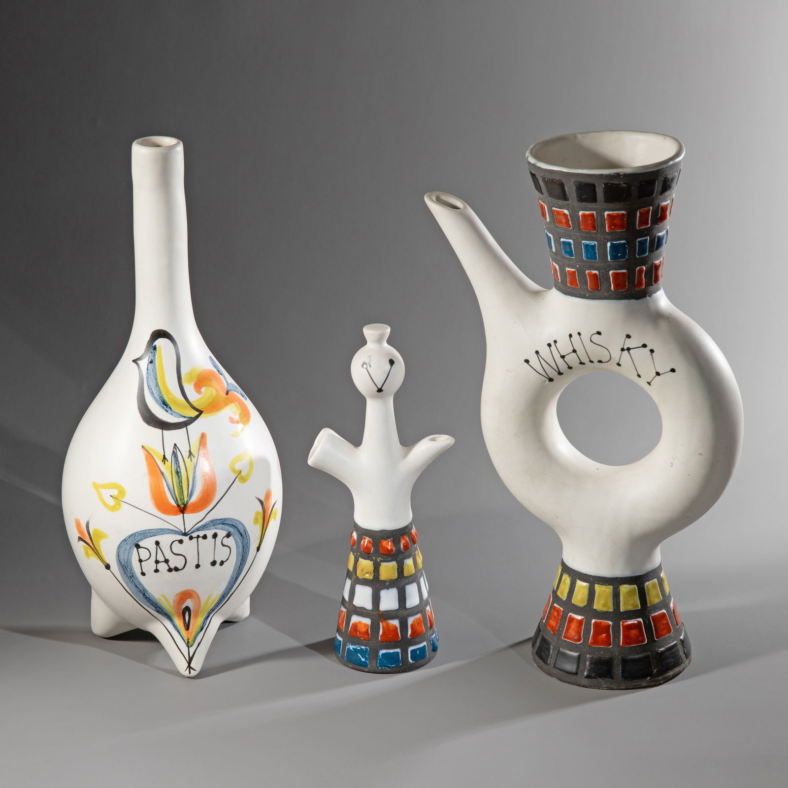 Roger Capron, 3 ceramic bottles: Ceramic, polychrome paint. Two bottles labeled 'Pastis' and 'Whisky'. Geometric decorations. Pastis bottle with stylized vegetable motifs and a depiction of a bird. H. 33 cm / H. 32 cm / H. 22 cm. Eac