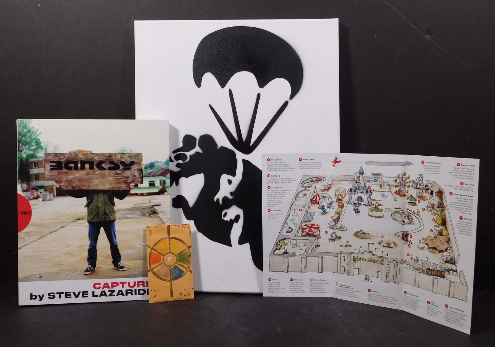 British Street Art: Dismaland Souvenirs: British Street Art: Dismaland Souvenirs. Stencil on canvas, Brochure, Free Money 1 cent, and Book "Captured" by Steve Lazarides. The canvas is 16 x 12 inches. Collection of Fountain Lake Farm