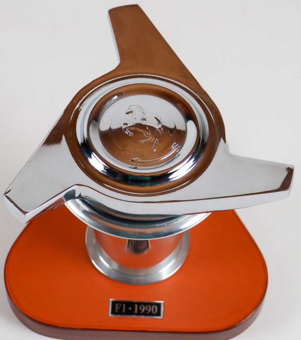 Ferrari 2-piece Desk Pieces from the 90s: F1 1990 intake manifold on wooden base covered with Schedoni leather, height: approx. 11.5 cm, as well as wheel hub cover