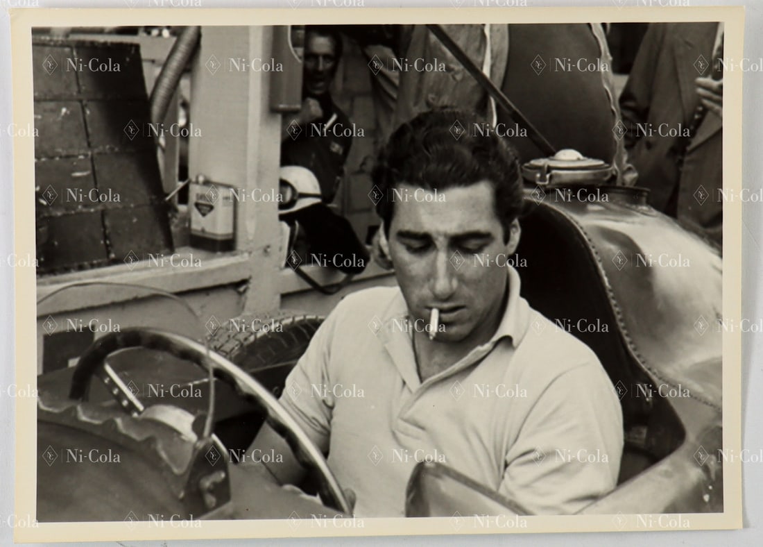 Ferrari Original Large-Format B/W Press Photo Alfonso de Po: Alfonso de Portago with a burning cigarette in the corner of his mouth at the wheel of his racing car in the paddock. 12.7 x 17.7 cm.