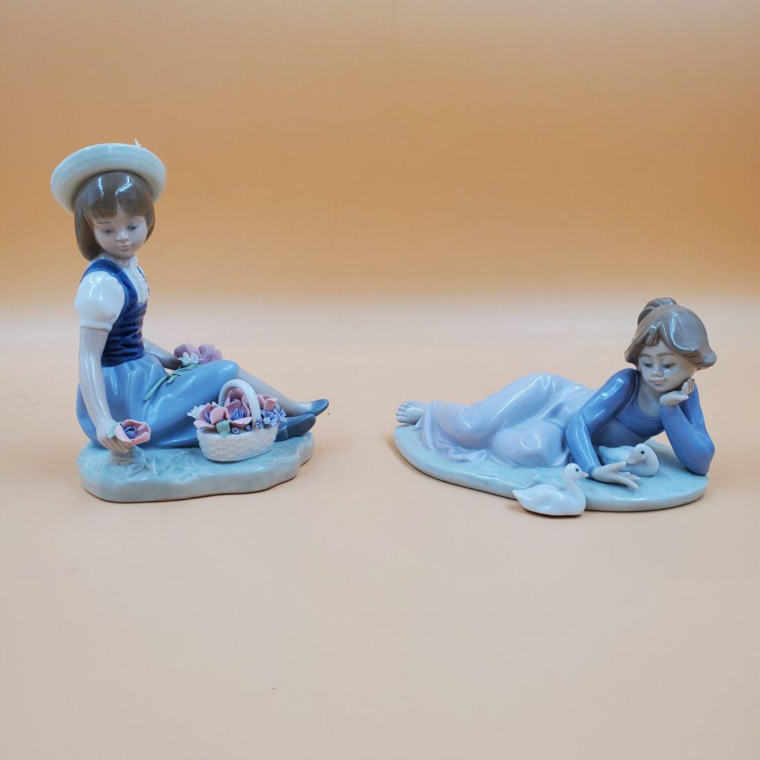 Pair of Lladro Porcelain Sculptures: Pair of Lladro Porcelain Sculptures. Depicts a girl picking flowers numbered 1287. and a girl playing with ducks numbered 1509. The girl picking flowers has her original box, but it is not in the best