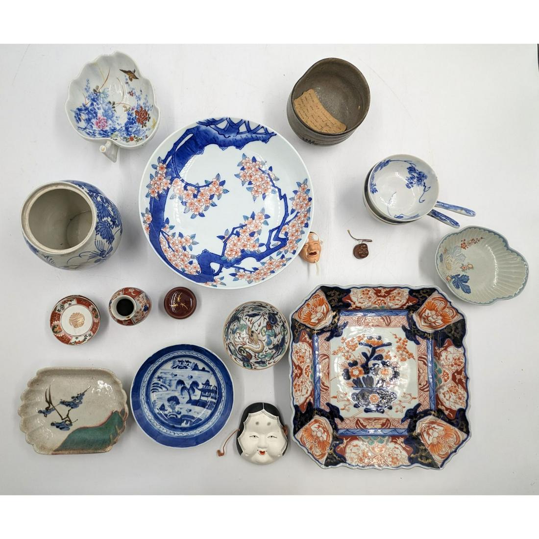 A Large Lot Of Various Japanese Decorative Objects, Mostly Porcelain, Approx. 19 Pieces: A Large Lot Of Various Japanese Decorative Objects, Mostly Porcelain, Approx. 19 Pieces. Includes a couple of decorative bowls, platters, netsuke faces, a vase, and a jar. Please carefully read our te
