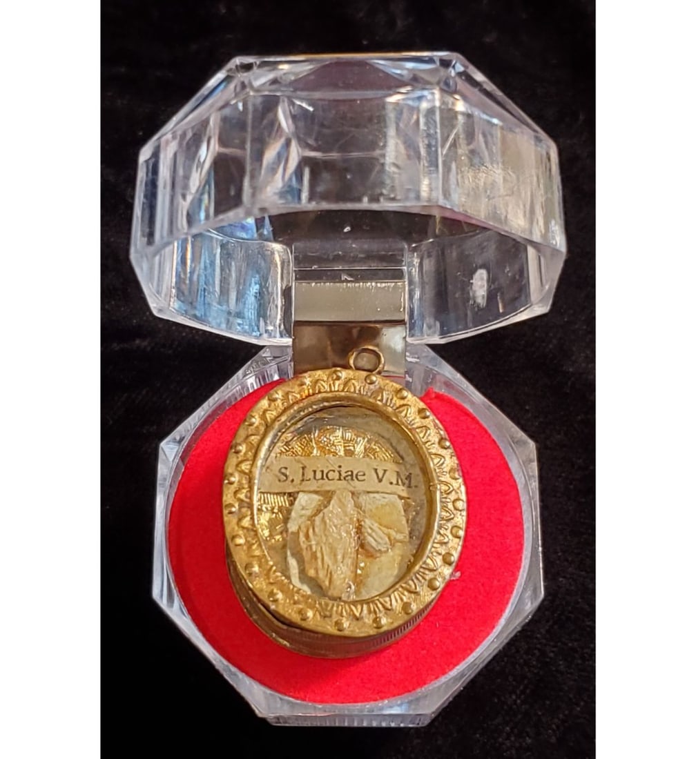 Large 1st Class Relic Of Saint Lucie, ex. Ossibus ( Bone ): Large 1st class relic of Saint Lucie, ex. Ossibus ( bone). The relic is contained in a very fancy oval theca. The theca is housed in a Gothic type acrylic presentation case. Saint Lucie is the patron 