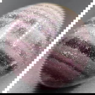 1-1/4" Agate Marble: 1-1/4" agate, purple bands cover 3/4 of the upper surface. While the base is lighter and visible forms can be seen on the interior. Near the top, there is a visible line or possible crack curving to t