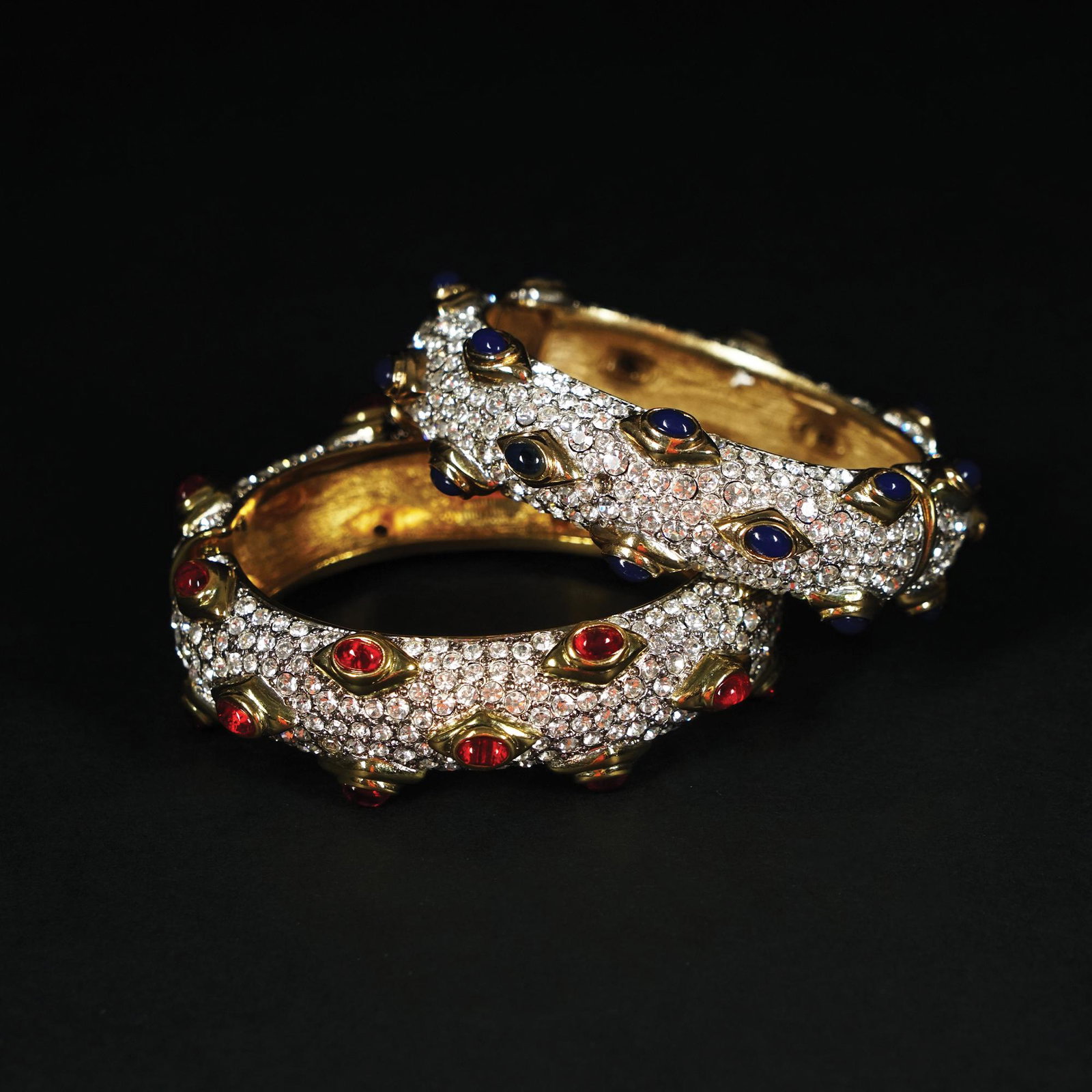 Kenneth Jay Lane: a pair of American gilt metal rigid bracelets with hinge with rhinestone pavÃ© and cabochon glass mounted on bezel, 20th centurym 5by6cm. each