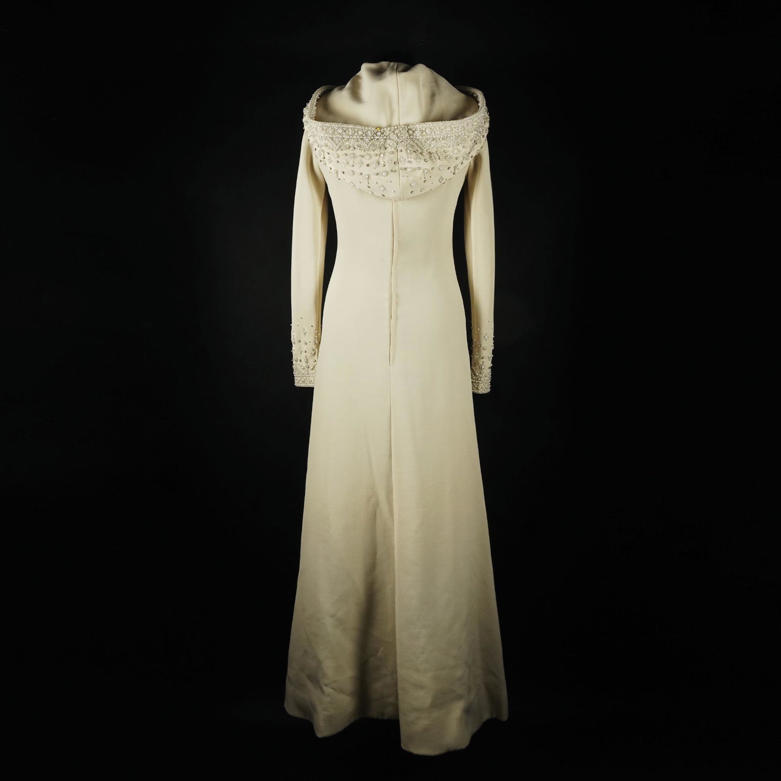 Mazzucchelli: a long dress with hood in ivory fabric with high cuffs, enriched by motifs embroidered in synthetic beads