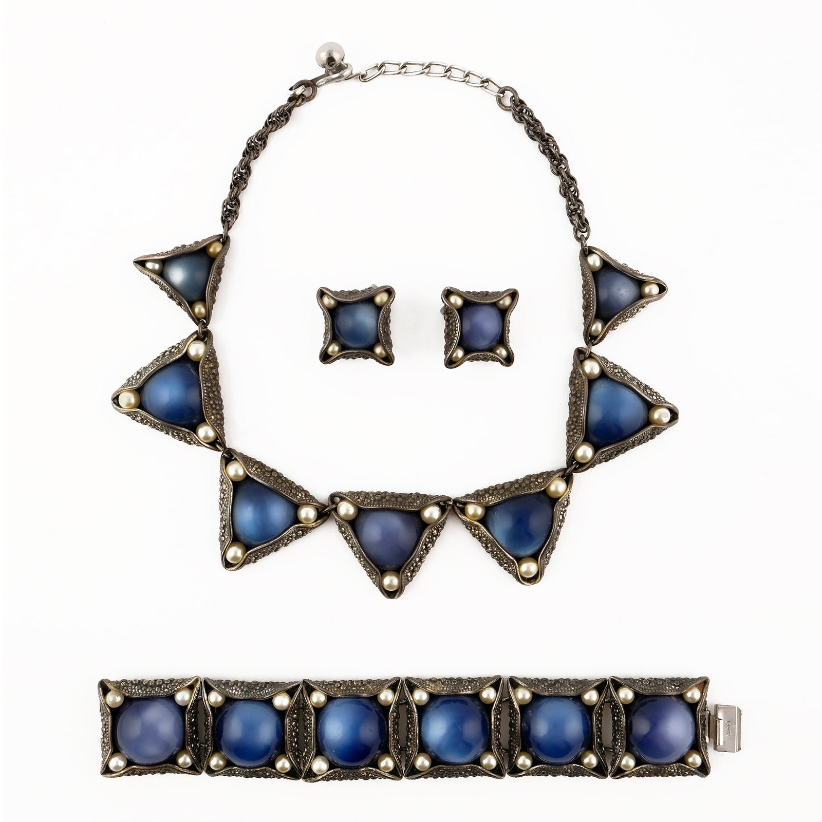 Napier: parure comprising a necklace, a bracelet and a pair of earrings in silvered and embossed metal, decorated with large cabochons in plastic material imitating sapphire.'50s, the l. cm. 39; the bracelet 