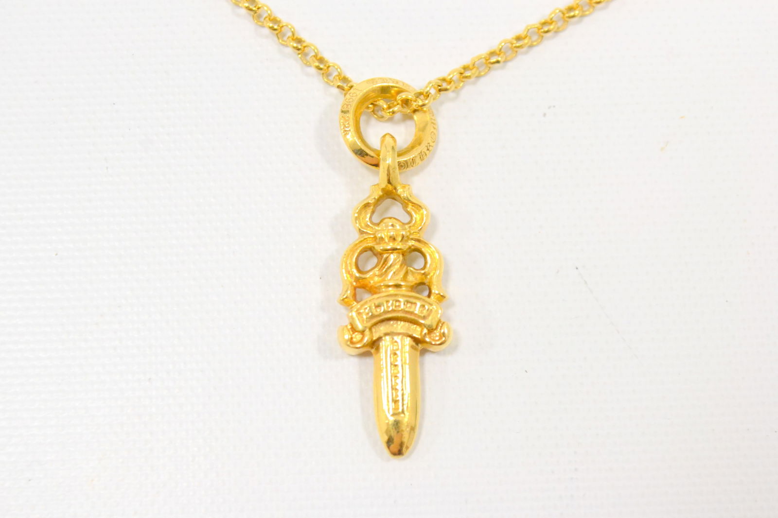 Chrome Hearts Dagger Pendant with Gold Chain: Description: Iconic Chrome Hearts dagger pendant necklace crafted in solid gold, showcasing the brand?s legendary gothic dagger motif suspended from a matching gold chain. The bold sculptural form and