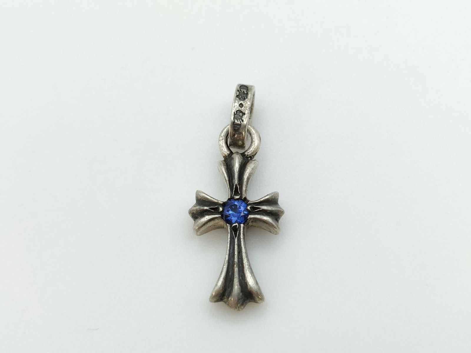 Chrome Hearts Blue Sapphire Silver Cross Charm Pendant: Description: Iconic cross charm pendant crafted in solid sterling silver, featuring Chrome Hearts? signature gothic cross silhouette accented by a vivid blue sapphire at the center. The sculptural for