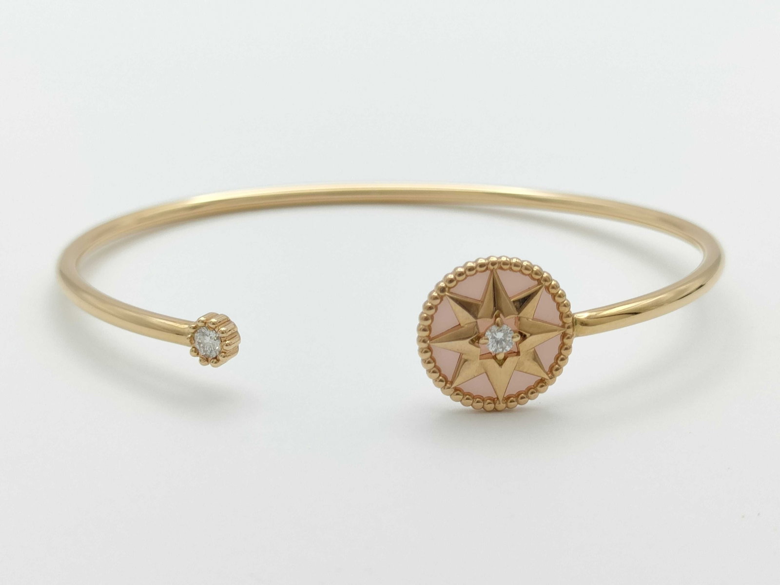 Dior Rose des Vents Pink Opal Diamond 18K Rose Gold Open Cuff Bracelet: Description: Elegant Dior Rose des Vents open cuff bracelet crafted in 18K rose gold featuring the Maison’s iconic compass rose motif. The medallion is set with soft pink opal and accented with 
