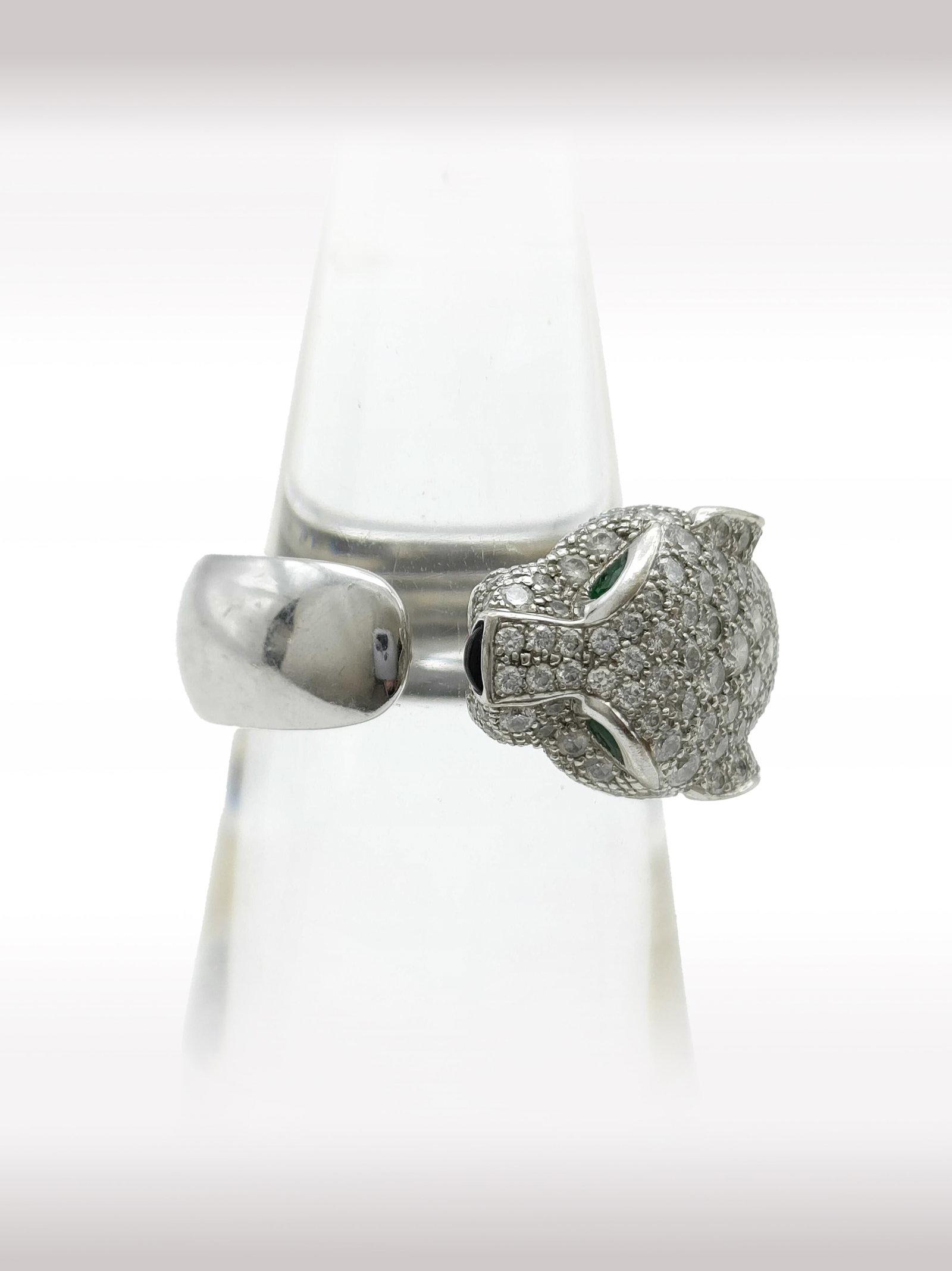 Cartier Panthere Diamond Pave Emerald Onyx 18K White Gold Ring: Description: Exceptional Cartier Panthere ring crafted in 18K white gold, featuring the Maison signature panther design fully accented with pave set diamonds. The eyes are set with vivid emeralds, whi