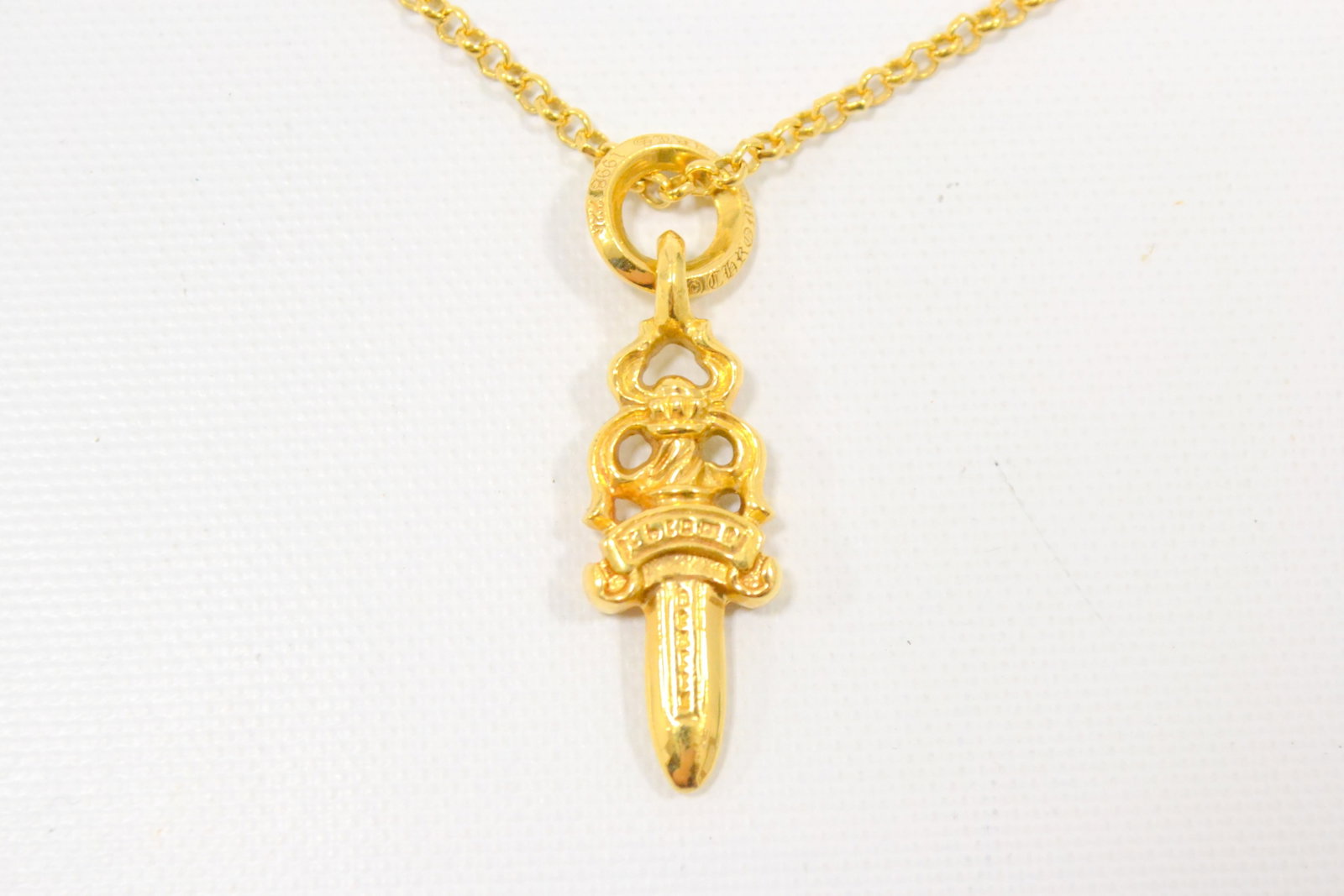 Chrome Hearts Dagger Pendant with Gold Chain: Description: Iconic Chrome Hearts dagger pendant necklace crafted in solid gold, showcasing the brand’s legendary gothic dagger motif suspended from a matching gold chain. The bold sculptural fo