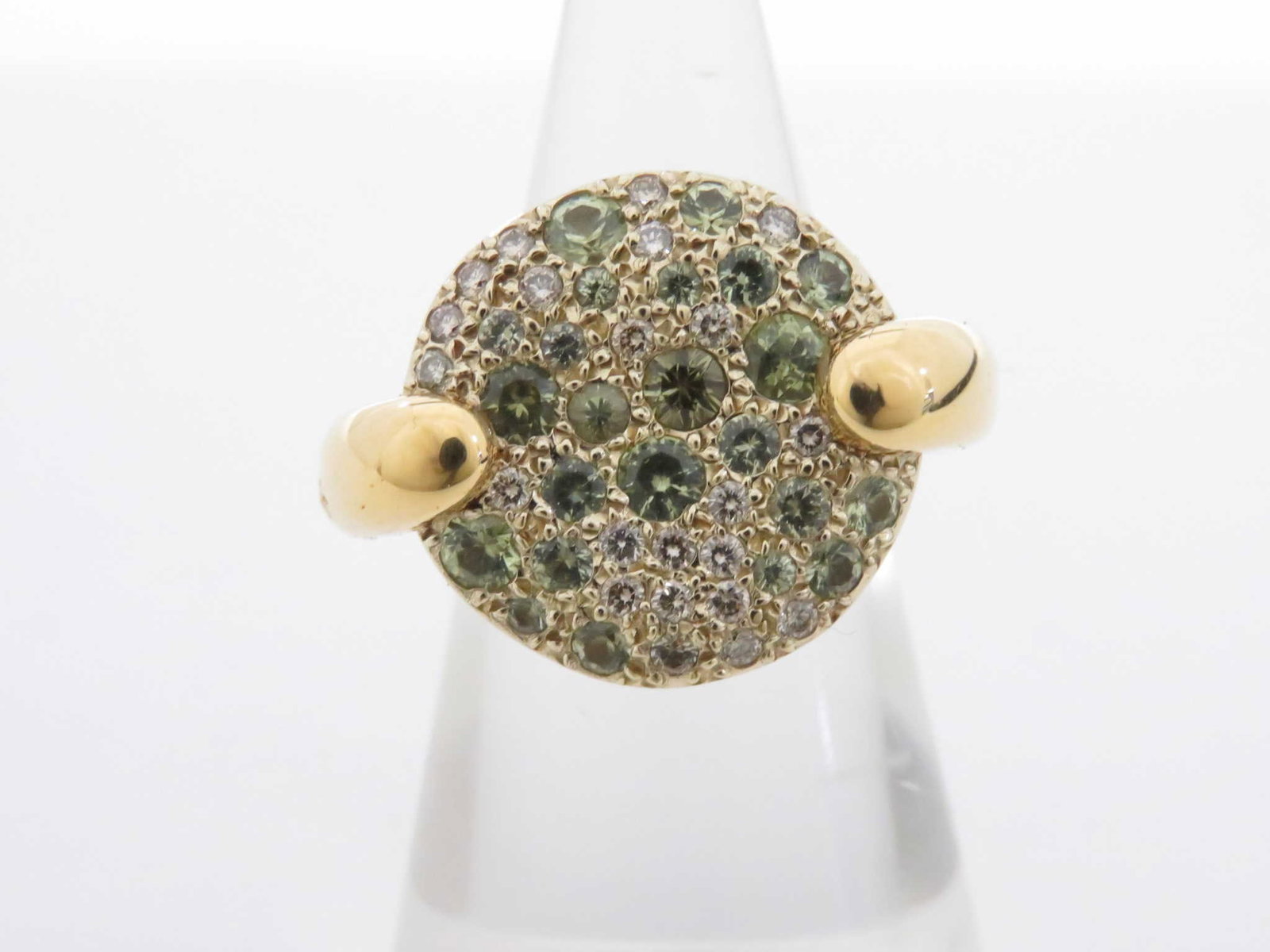 Pomellato Green Sapphire Diamond 18K Yellow Gold Pave Ring: Description: Striking Pomellato ring crafted in 18K yellow gold featuring a circular pave cluster of green sapphires accented with diamonds. The dome-shaped design showcases a rich mix of green sapphi
