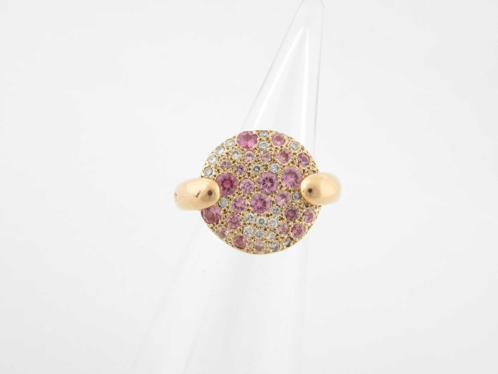 Pomellato Sabbia Pink Sapphire Diamond 18K Yellow Gold Ring: Description: Elegant Pomellato Sabbia ring crafted in 18K yellow gold featuring a circular pave cluster of pink sapphires accented with sparkling diamonds. The dome shaped design creates a soft textur