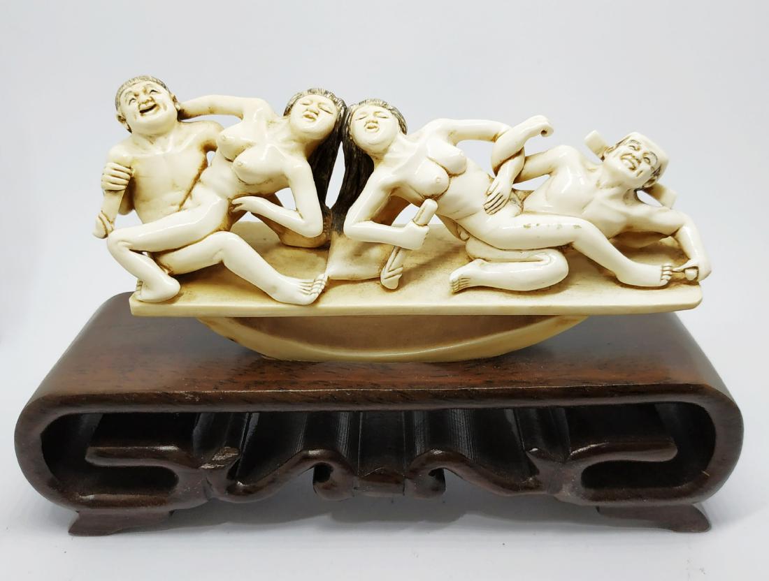 Erotica - multiple participants, Japanese bone carving: Four figures playing on a swing holding in their hands sexual organs. A high quality bone carving, decorated with black details. Signed by a master in red. In a very good condition, on a matching wood