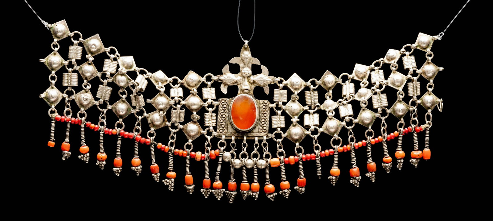 Silver and coral headdress for a bride Islamic Turkmen: The Turkmenistan headdress is made up of hammered and wrought silver elements. A central plaque in the center is set with a large carnelian stone. The bottom of the head piece is adorned with red and 