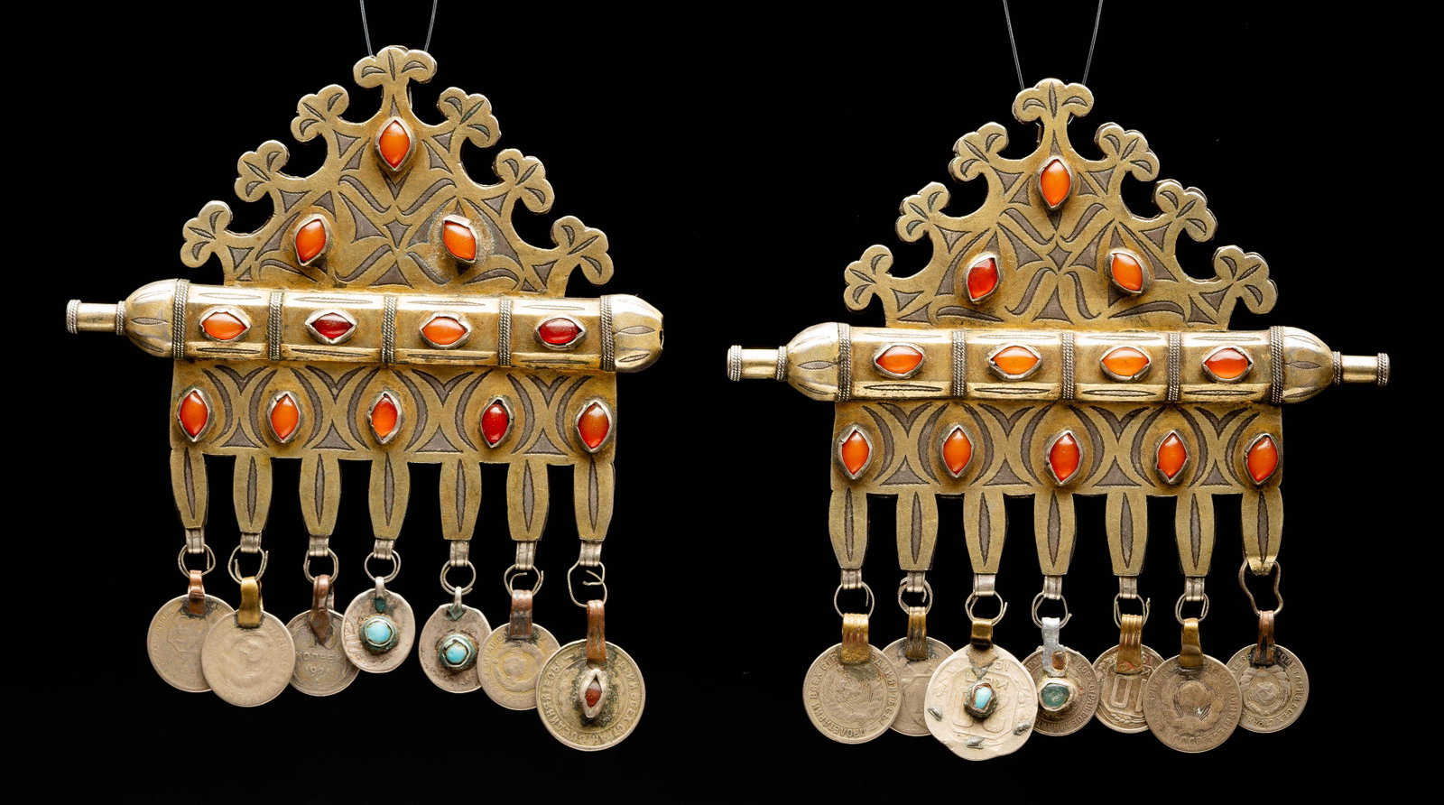 Two identical gilt Tumar pendants-19th c Turkmenistan: The two pendants are finely cut and engraved in organic design. Carnelian stones set throughout Upper part designed in altered triangular form. The middle of the piece is the cylindrical amulet holder