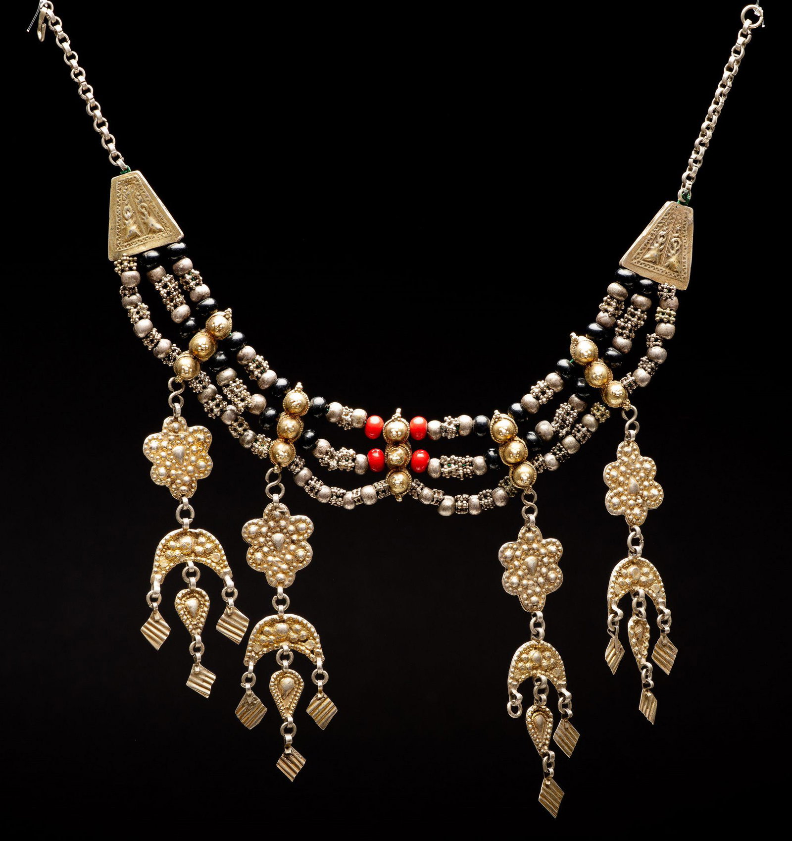 A gilt silver crescent necklace Middle East Islamic: The necklace is comprised of black beads and red beads and various silver ornaments. Hanging from the bottom are floral pendants and Islamic crescent pendants. punched, cast, soldered, gilded, cast le