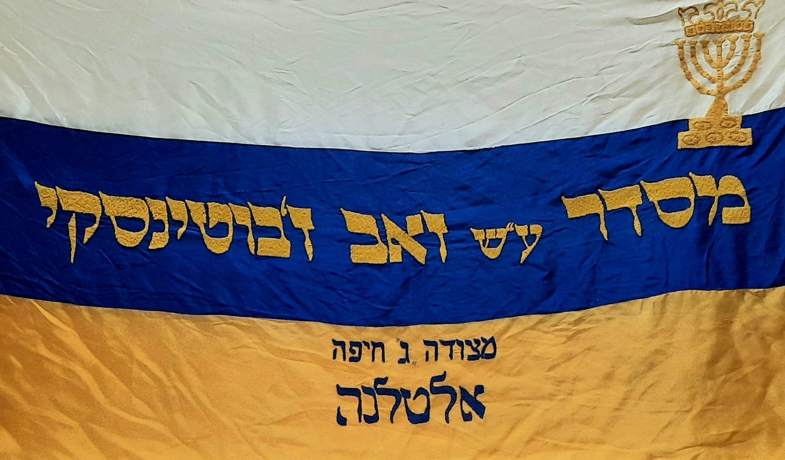 Ze'ev Jabotinsky Medal Bronze Beitar Menorah on Silk: Embroidered fabric flag. Added are wood poles, deconstructable into 3 parts for lifting. And a bronze Lamp, height: 22 cm, width: 18 cm. Measurements: 166 cm length. 93 cm width. <