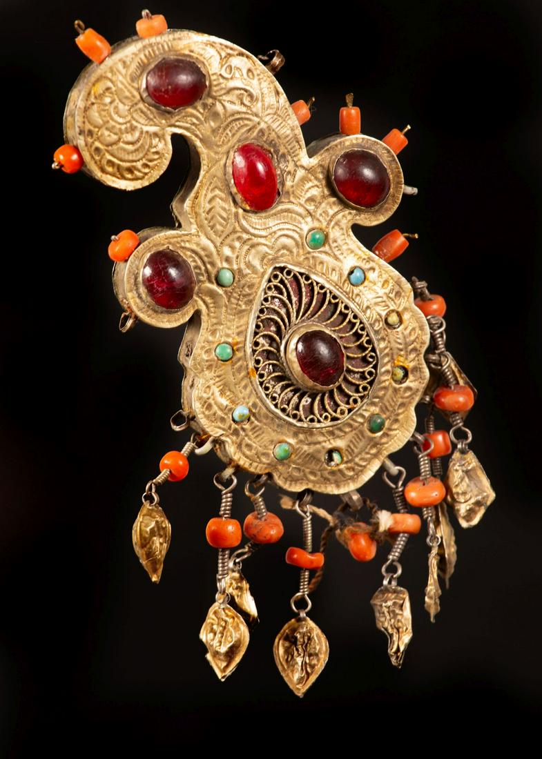 A fine gilt silver pendant - Uzbekistan - 1880-1900: The ornament is set with turquoise (some missing) and red cabochon and decorated with fine hammer work and filigree. Tassels with corals and gilt silver elements hang down from the main body. (some mi