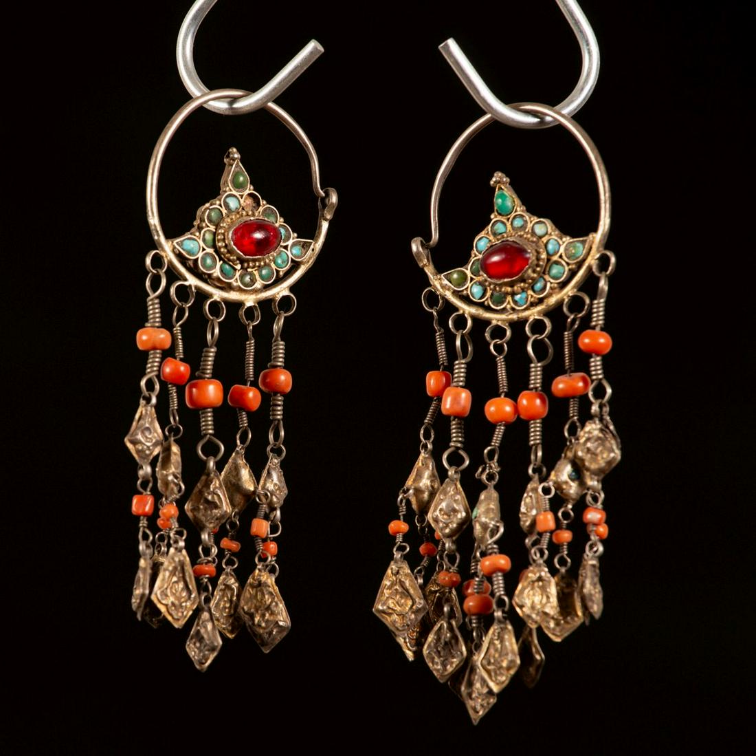 A pair of gilt silver and coral earrings - Uzbekistan -: Each hoop is decorated with a large two-sided rosette-shaped element inset with turquoise and a red cabochon in center. Five typical strands hang from the bottom of the hoop decorated with coral beads