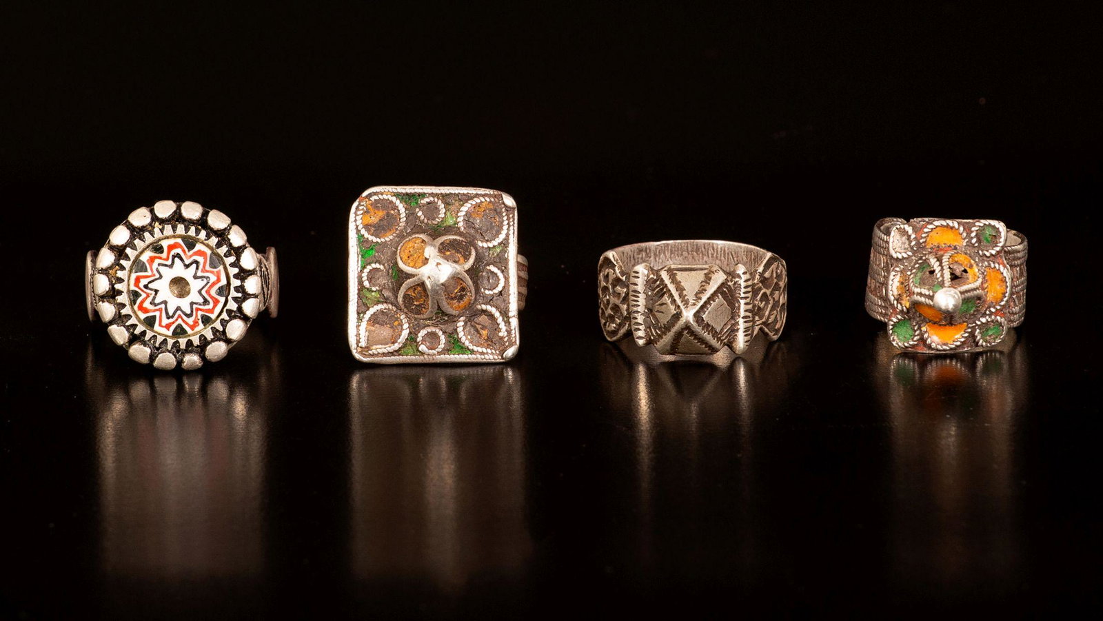 A lot of four silver rings - Morocco: 1. A silver engraved ring with a square plaque on top with a dome. decorated with filligree and signs of emnamel paint. 2. A silver engraved wide ring with a square plaque on top with a dome. decorate