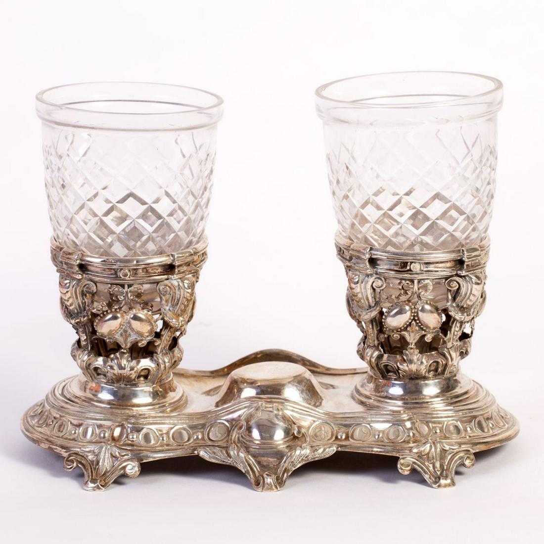 Silver Cup Stand: Cup stand made of Sterling Silver decorated with lovely sawing and embossing. Has two accompanying polished silver cups. Stands on six legs. Dimensions: 16X25.5 cm. Height: 11 cm. Weight (of silver):