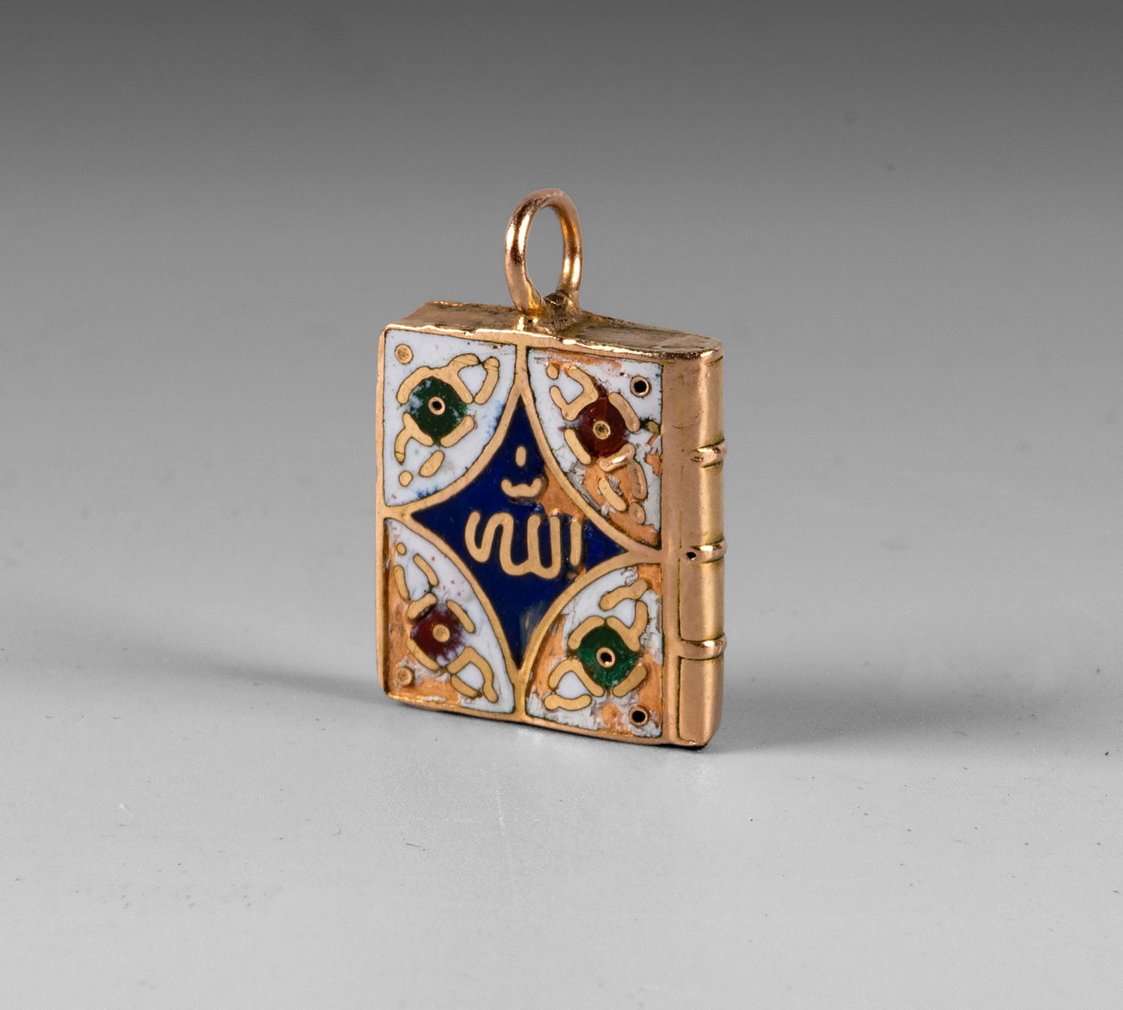 A 14k Gold and Enamel Unique Miniature Quran Book-Shaped Pendant: A 14k Gold and Enamel Unique Miniature Quran Book-Shaped Pendant Designed as a Quran book cover, both sides are adorned with colorful selective enamel and Arabic calligraphy. The interior is hollow.